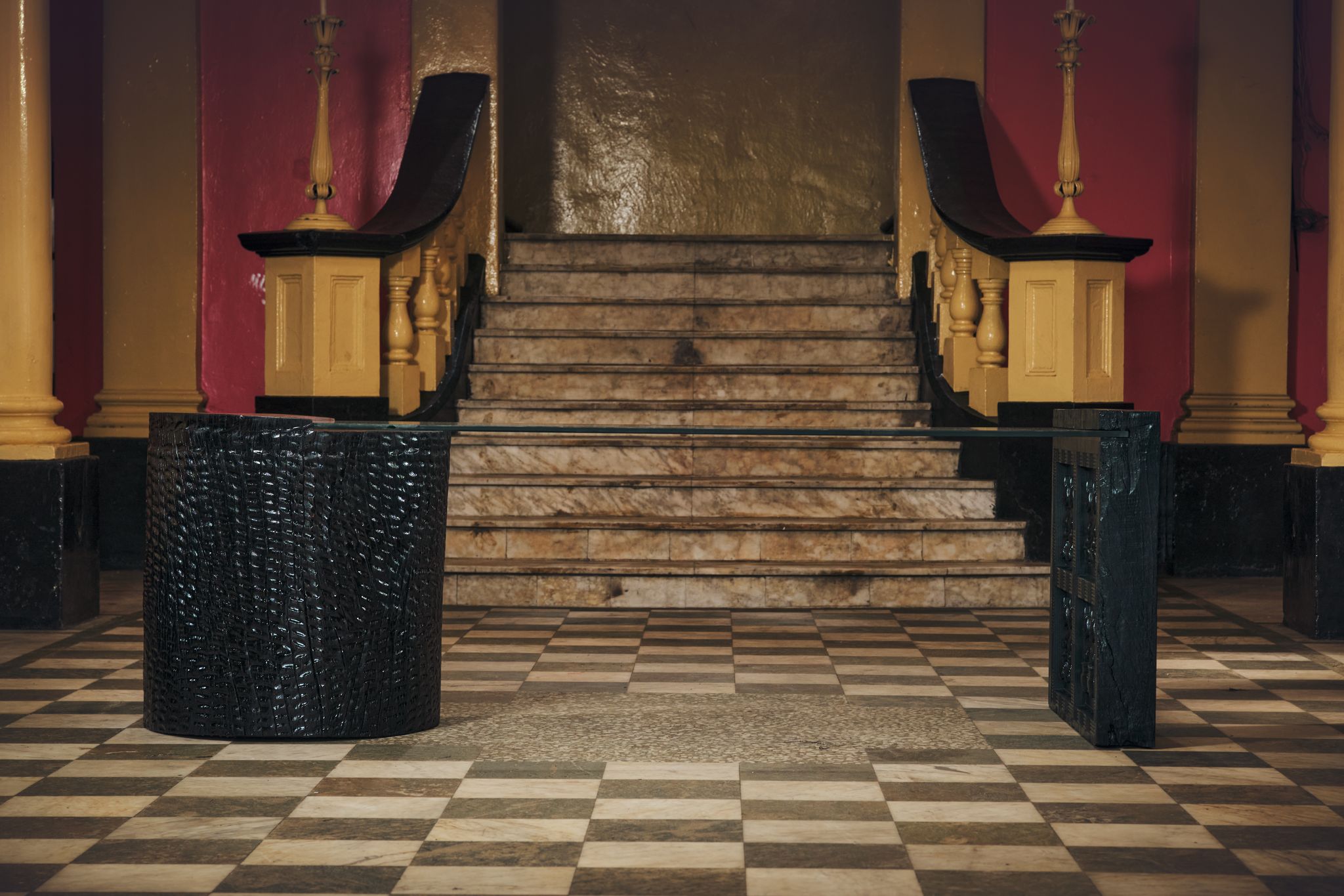 The table in the hall: a carved round base and a carved end panel joined by a sheet of glass